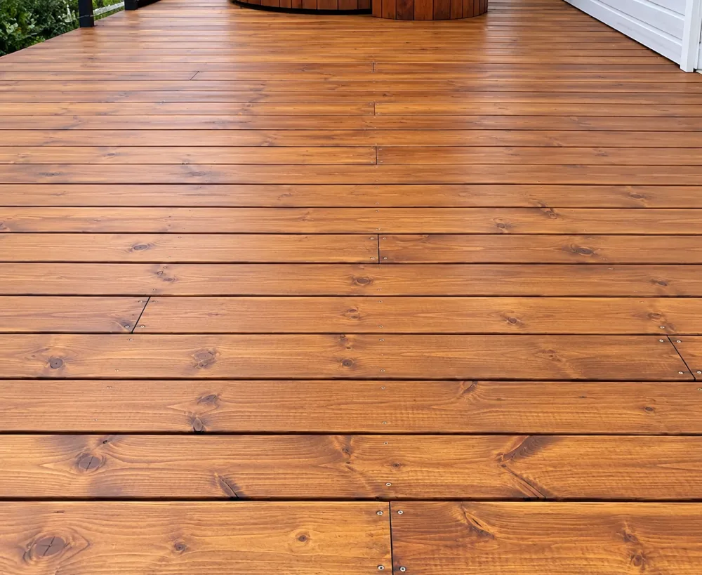 Faut-il attendre un an avant de teindre une terrasse en bois traité ? Ce qu’il faut vraiment savoir 2 Vue plongeante sur une terrasse en bois composée de planches horizontales, avec vis visibles et nœuds du bois.